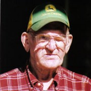 Elderly man with glasses, a green trucker hat, and a red plaid shirt